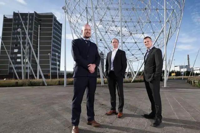 Three members of the Profast Group standing in front of the 'balls of the falls' in Belfast